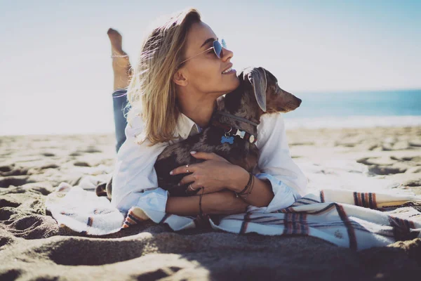 Улыбающаяся Блондинка Модном Наряде Мягко Обнимает Свою Собаку Расслабляясь Песчаном — стоковое фото