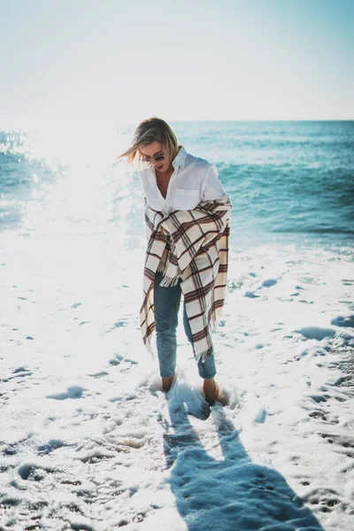 해변을 맨발로 의물을 즐기는 금발의 여인을 안경을 평상복을 주말을 바다에서 스톡 사진