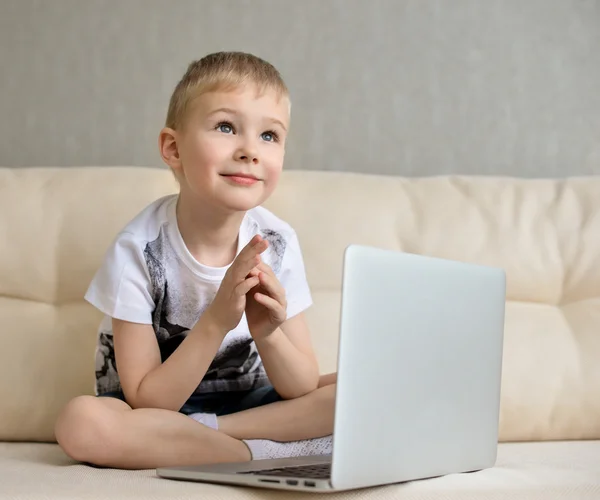 Niño pequeño sentado con el ordenador portátil en el sofá en casa —  Fotos de Stock