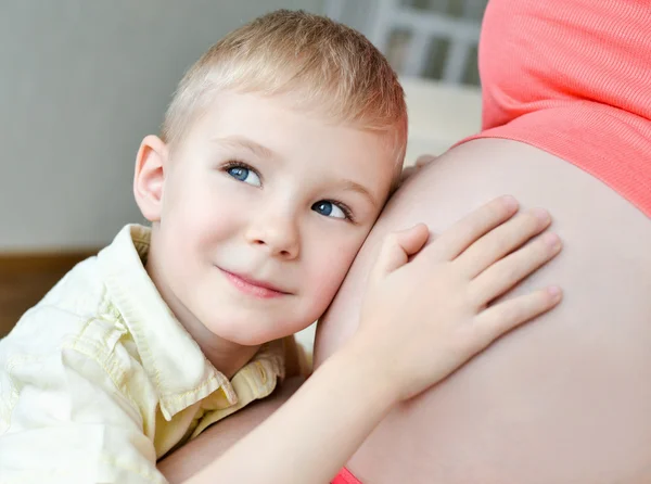 Little boy listening pregnant belly of his mother, at home Stock Image