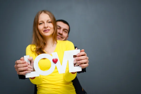 Hermosa pareja sonriente sosteniendo la palabra AMOR, de pie juntos sobre fondo gris — Foto de Stock