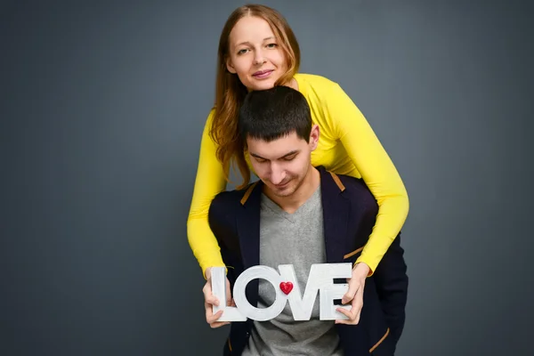 Krásný úsměv pár hospodářství slovo láska, stáli na šedém pozadí — Stock fotografie