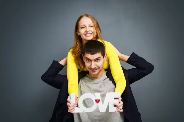 Vackert leende par innehav ordet kärlek, står tillsammans på grå bakgrund — Stockfoto