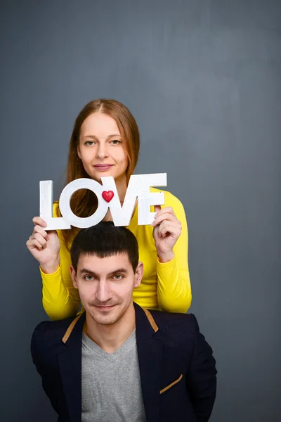 Hermosa pareja sonriente sosteniendo la palabra AMOR, juntos sobre fondo gris — Foto de Stock