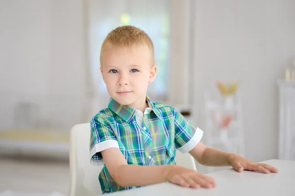 Маленький улыбающийся мальчик сидит за столом — стоковое фото