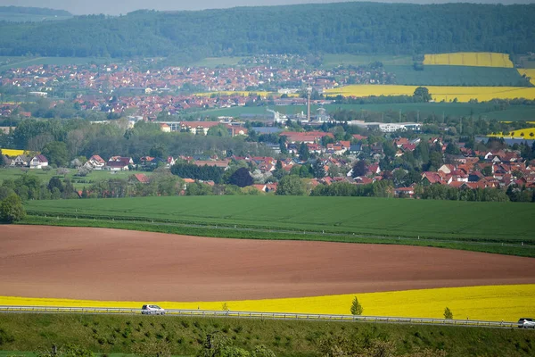 GERMANY - AUGUST 2015: Panorama of the city with red roofs, yellow rapeseed field, the road along the fields. — Stockfoto