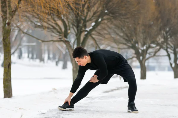 Молодой человек делает растяжку в утренних упражнениях, делает фитнес на открытом воздухе зимой в снегу. — стоковое фото