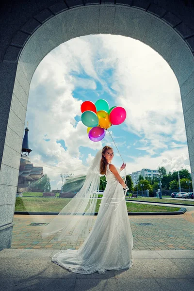 Женщина в длинном белом платье с шариками в руках на фоне неба с облаками. — стоковое фото