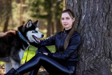 İri yapılı güzel bir kız ormanda bir ağacın yanında oturuyor. Arka plan, doğal ışıklandırma.