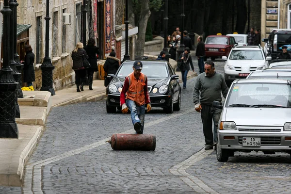 AZERBAIJAN, BAKU - November 2009: Ein uniformierter Arbeiter rollt eine Gasflasche mit dem Fuß die Straße entlang.. — Stockfoto