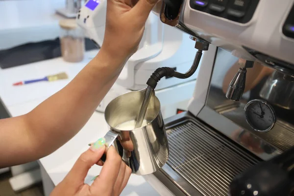 Minsk. Bielorrússia - 06.06.2021: Mulher barista em uma caneca de ferro espumas leite de café. — Fotografia de Stock