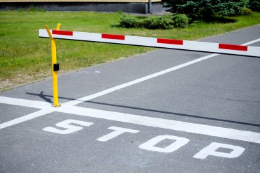 Yolda bir bariyer ve dur tabelası var. Beyaz-kırmızı bariyer yolda. Yol kenarları boyunca yeşil.