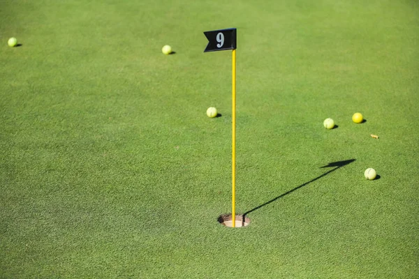 Flag in a golf hole on a background of green grass and golf balls. Golfing, golf hole. — Stock Photo, Image