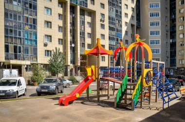 Nur-Sultan. Kazakistan: 04.09.2013 - Sarı bir konut binasında çocukların oyun alanı, mavi gökyüzüne karşı bir yerleşim alanı. Nur-Sultan. Kazakistan.