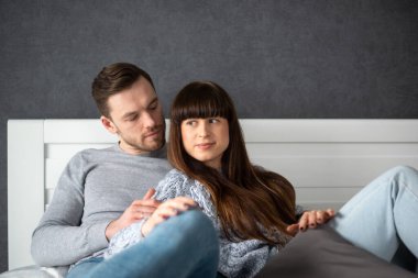 Genç bir adam ve kadın beyaz bir başlıkla yatakta sarılıyorlar..