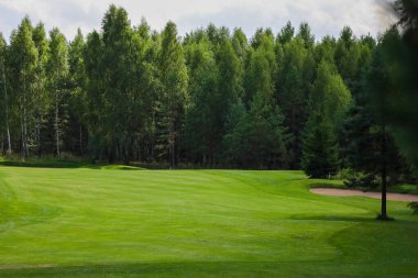 Golf sahası, manzara, arka planda yeşil çimenler ve bulutlu parlak bir gökyüzü.