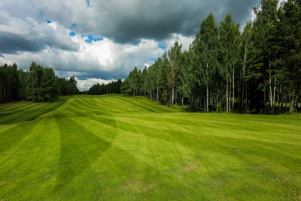 Campo de golfe, paisagem, grama verde no fundo de uma floresta e um céu brilhante com nuvens — Fotografia de Stock