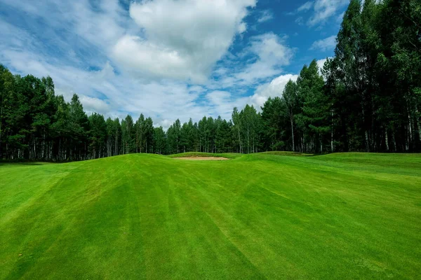 Golfové hřiště, krajina, zelená tráva na pozadí lesa a jasná obloha s mraky — Stock fotografie