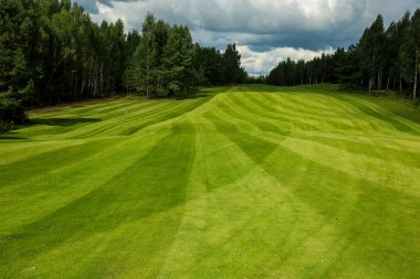 Golf sahası, manzara, arka planda yeşil çimenler ve bulutlu parlak bir gökyüzü.