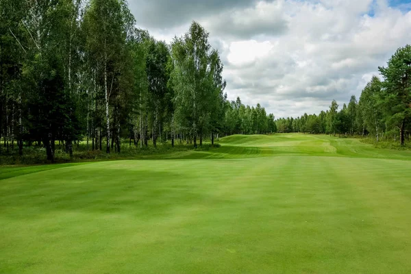 Golfové hřiště, krajina, zelená tráva na pozadí lesa a jasná obloha s mraky — Stock fotografie