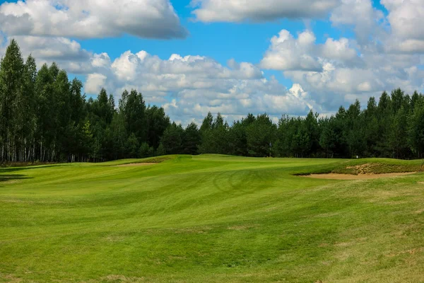 Campo de golf, paisaje, hierba verde en el fondo de un bosque y un cielo brillante con nubes —  Fotos de Stock