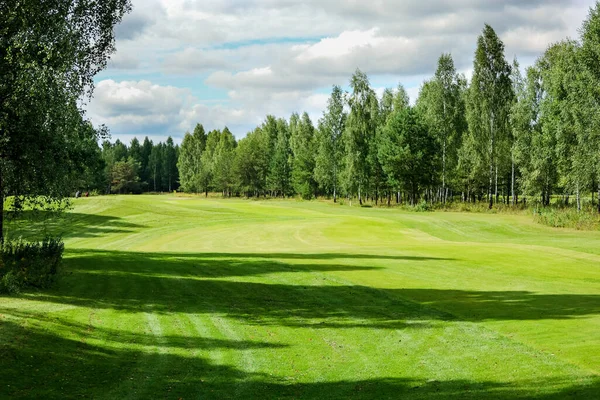 Campo de golf, paisaje, hierba verde en el fondo de un bosque y un cielo brillante con nubes —  Fotos de Stock