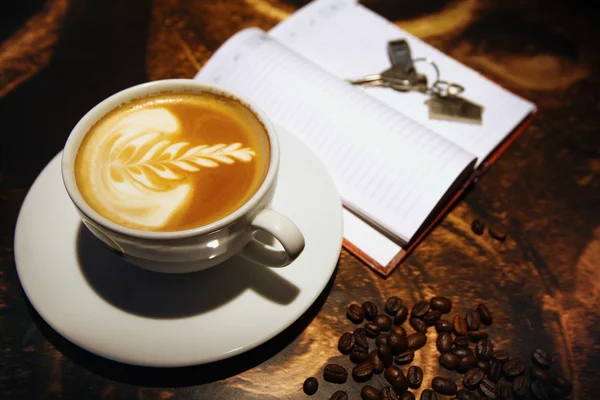 Xícara de café na mesa e chaves no caderno — Fotografia de Stock