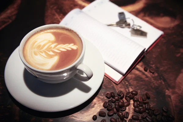 Tasse Kaffee am Schreibtisch und Schlüssel am Notizbuch — Stockfoto