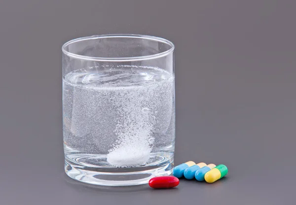 Piller och glas vatten på grå bakgrund — Stockfoto