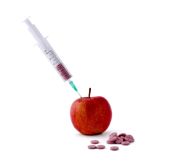Lékařskou stříkačkou nezdolnou pilulky a červené jablko, ležící na stole, izolovaných na bílém pozadí — Stock fotografie