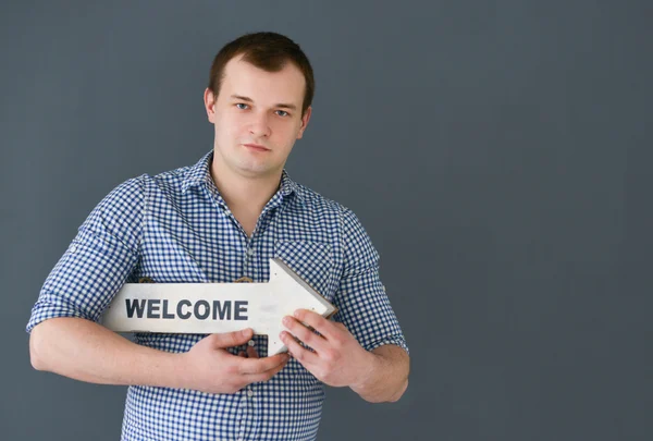 Young man holding welcome board banner, standing on dark background