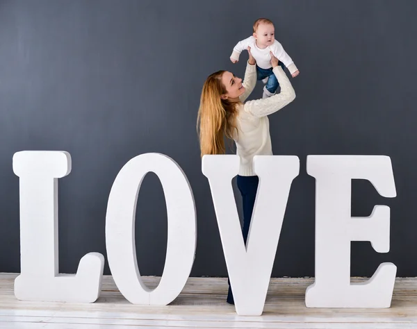 Stående lycklig mor och barn, på grå bakgrund nära stora bokstäverna i ordet kärlek — Stockfoto