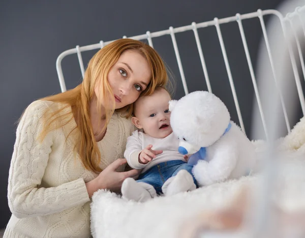 Ung mamma och baby ligger på sängen leker med en leksak Björn — Stockfoto