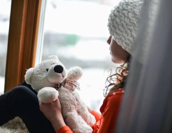 Leuk meisje met lange haren zitten alleen in de buurt van venster op een vensterbank — Stockfoto