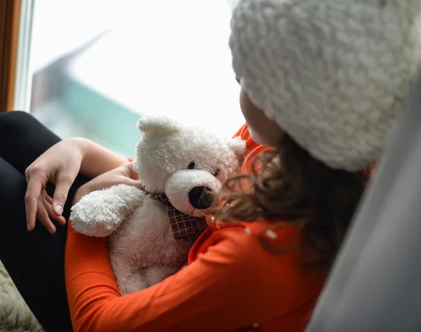 Leuk meisje met lange haren zitten alleen in de buurt van venster op een vensterbank — Stockfoto