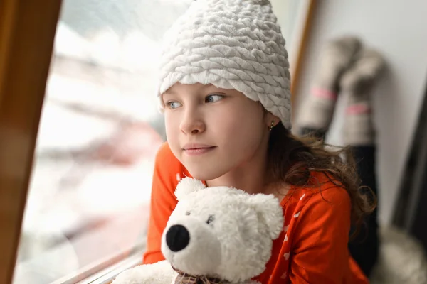 Leuk meisje met lange haren zitten alleen in de buurt van venster op een vensterbank — Stockfoto