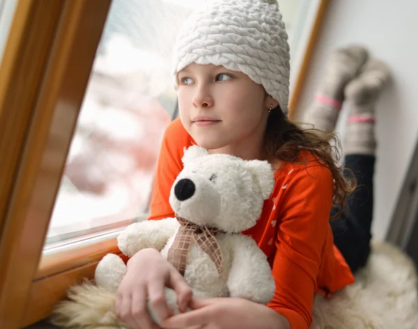 Leuk meisje met lange haren zitten alleen in de buurt van venster op een vensterbank — Stockfoto