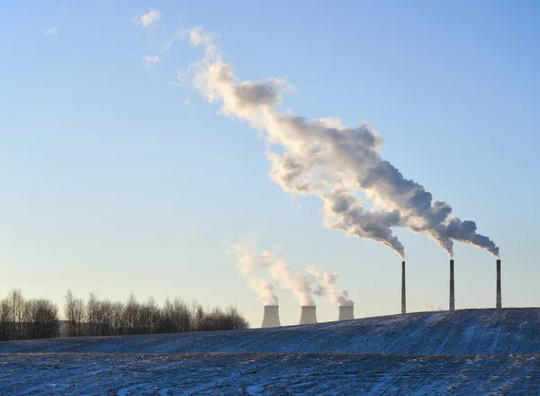 Winterlandschap met fabriek schoorstenen en wolken tegen de zon — Stockfoto