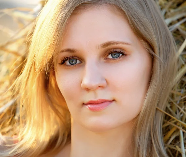 Closeup retrato de uma jovem menina bonita sentada no feno no campo — Fotografia de Stock