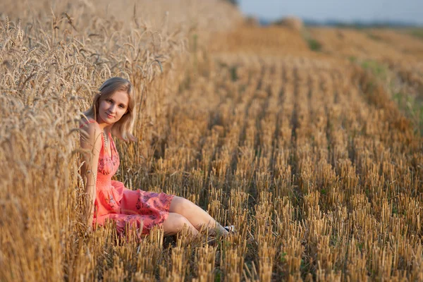 Jovem menina bonita sentada no feno no campo — Fotografia de Stock