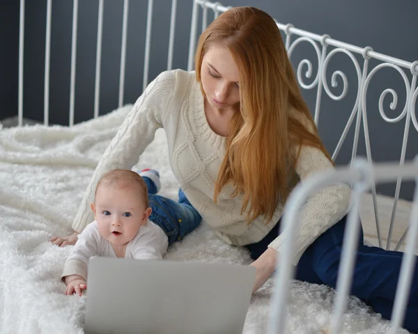 Woman with baby and laptop sitting on bed at home — Stock Photo, Image