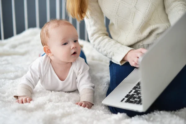 Woman with baby and laptop sitting on bed at home — Stock Photo, Image