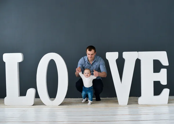 Feliz padre llevando hijo aislado sobre fondo gris cerca de grandes letras de la palabra amor —  Fotos de Stock