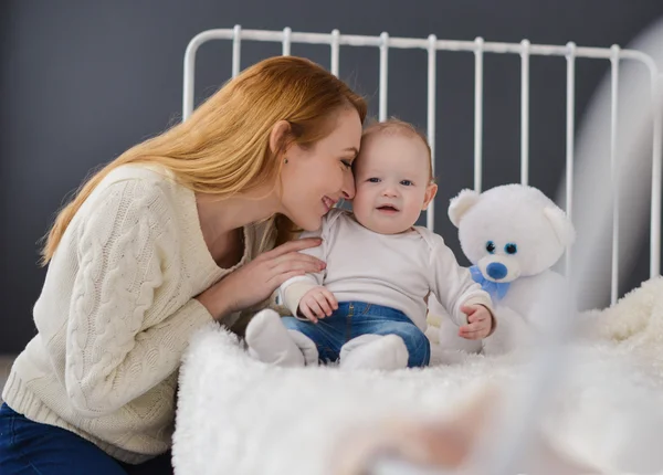 Young mother and baby lying on the bed playing with a bear toy — Stock Photo, Image