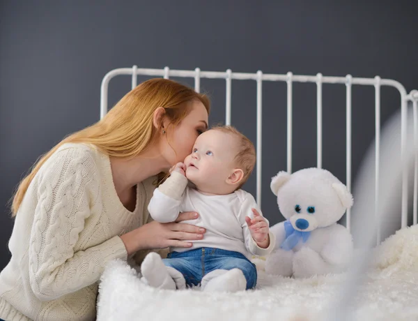 Young mother and baby lying on the bed playing with a bear toy — Stock Photo, Image