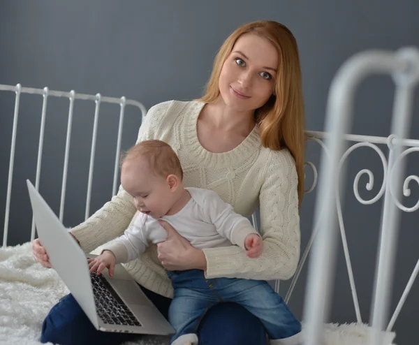 Kobieta z dzieckiem i laptopie siedząc na łóżku w domu — Zdjęcie stockowe