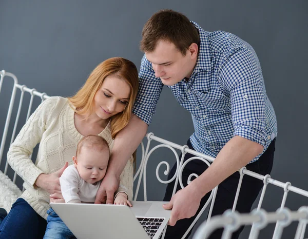 Mother ,father with baby and laptop sitting on bed at home — Stock Photo, Image