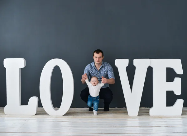 Szczęśliwy ojciec prowadzenia syna na białym tle na szarym tle w pobliżu dużych liter słowa miłości — Zdjęcie stockowe