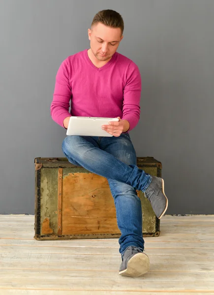 Attraktiver junger Mann sitzt auf einem alten Koffer und hält Flugzeugtisch — Stockfoto