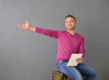 Eski bir bavul ve uçak-tablo tutan çekici genç adam oturur